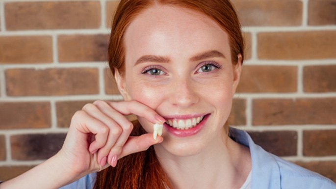 A smiling red-headed woman holding an extracted tooth 