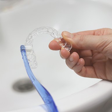 Patient cleaning clear aligner with toothbrush in sink